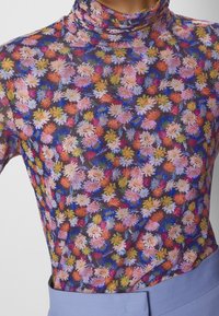 Długi rękaw, golfowy top wykonany z przezroczystego materiału, z wyrazistym kwiatowym wzorem w kolorach różowym, pomarańczowym i niebieskim na ciemnym tle.