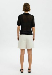 Svart kortärmad skjorta med krage och ribbad textur, kombinerat med ljusbeiga shorts. Sandaler med en enkel design fulländar outfiten.