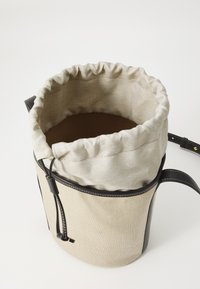 Geantă tip borsetă din pânză, cu închidere prin șnur, corp de culoare bej, margine din piele neagră și curea ajustabilă. Interior căptușit cu material de culoare marron.