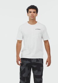 Hvid kortærmet t-shirt med rund hals, der har et diagonalt sømdesign og et sort "TERREX"-logo på venstre bryst. Blødt, glat stof.