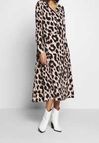 Midi sukienka w leopardzie w jasnoróżowym i czarnym kolorze, z kołnierzykiem i długimi rękawami, w połączeniu z białymi kowbojkami.