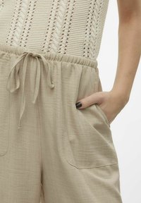 Pantalons en mélange de lin beige avec taille élastique et cordon de serrage. Comprend deux poches latérales et un tissu doux et texturé.