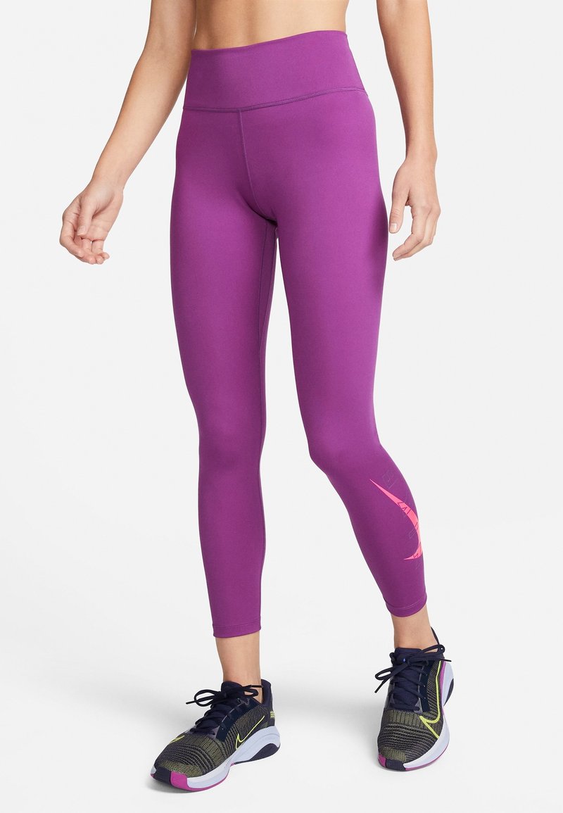 Fialové legíny s vysokým pasem a hladkou texturou, na boku s růžovým logem swoosh a nošené s tmavými sportovními botami.