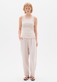 Heled hall ribato top, mis on kombineeritud vabalt involveeritud kreemide laiade pükstega. Mudel kannab musti flip-flops'e. Lihtne, minimalistik disain.