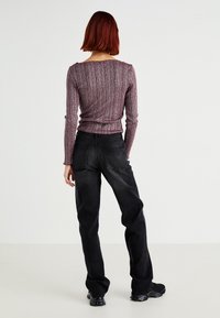 Long-sleeve, ribbed knit top in purple and pink hues, paired with high-waisted black jeans. Simple design with a fitted silhouette.