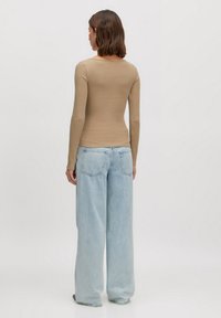 Langemouwen, aansluitend beige top gecombineerd met lichtblauwe, wijde jeans. De top heeft een eenvoudige uitsnijding; de jeans hebben achterzakken.