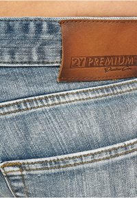 Lyseblå denimjeans med brun lærlapp; preget synlige sømmer og en baklomme. Teksten på lappen er "2Y PREMIUM."