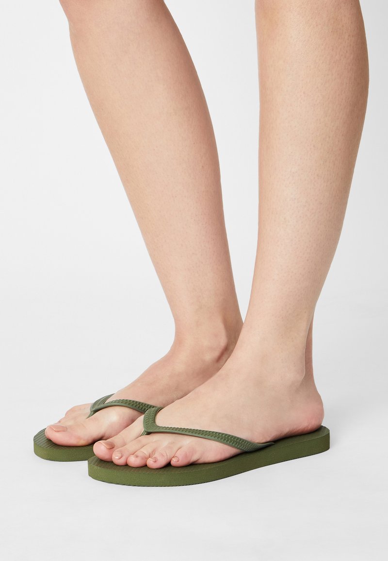 Grønne flip-flops med en teksturert gummisåle og tynne V-formede remmer. Designet har en flat profil og stil med åpen tå.