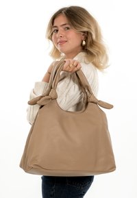 Beige Lederhandtasche mit glatter Textur, ausgestattet mit verknoteten Griffen und einem geräumigen, abgerundeten Design. Geeignet für den Alltag oder legere Anlässe.