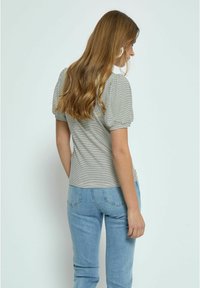 Short-sleeve striped top with a fitted design. Soft fabric, subtle puffed shoulders, and neutral colors paired with light blue jeans.