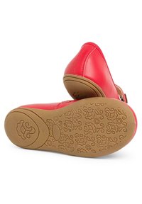 Zapatos de cuero rojo con punta redondeada, que presentan una suela de goma marrón texturizada grabada con patrones florales. Detalle de correa ajustable y hebilla.