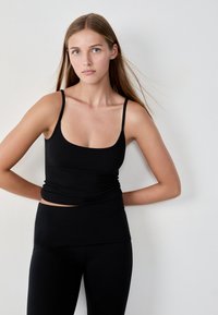 Débardeur noir ajusté avec des bretelles fines, doté d'un décolleté en cœur et de détails froncés à la taille, associé à un legging taille haute assorti.
