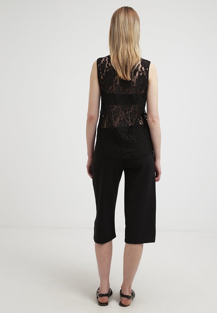 Top in pizzo nero con un design a righe verticali, abbinato a pantaloni neri cropped dalla vestibilità ampia. Texture liscia; senza maniche, silhouette rilassata.