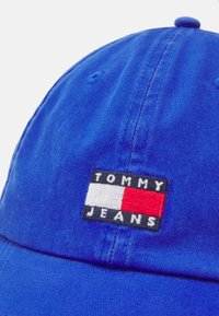 Zila kokvilnas beisbola cepure ar izšūtu "TOMMY JEANS" logo, kas satur melnu, baltu un sarkanu krāsu. Strukturēta auduma, apaļa forma.