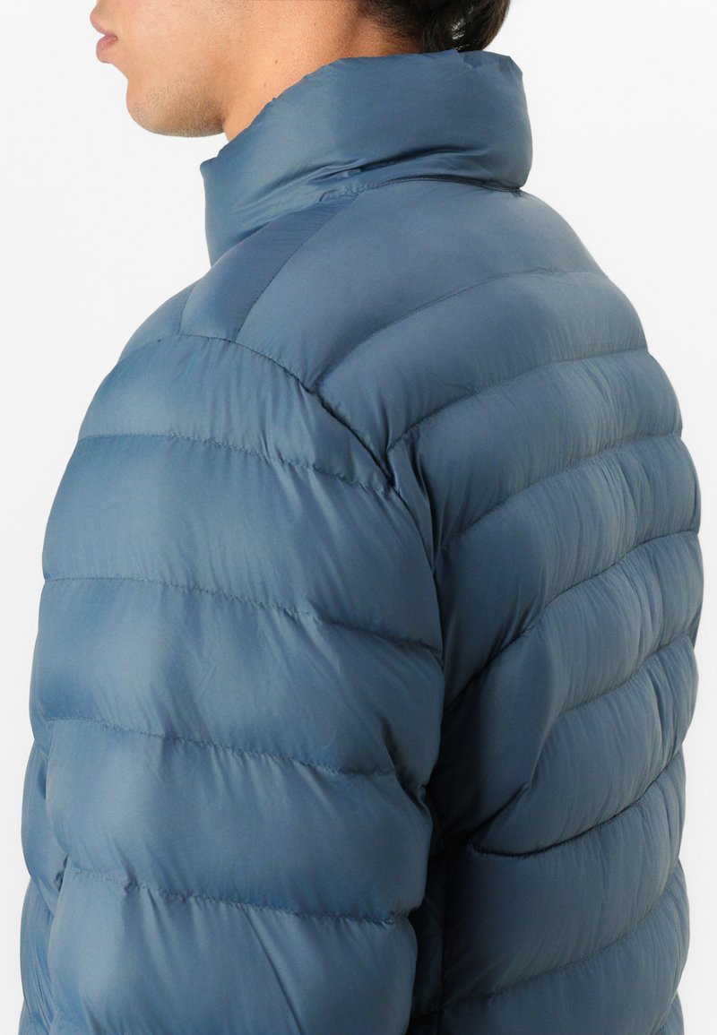 Chaqueta de plumas en azul oscuro, con un alto cuello, patrón acolchado y exterior suave. Material ligero con un diseño elegante.
