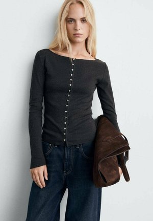 Top fitted a maniche lunghe grigio scuro con scollo a barca e una fila di bottoni rotondi lungo la parte anteriore, abbinato a jeans a gamba larga blu scuro e borsa marrone.