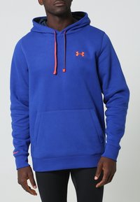 Niebieska bluza z kapturem wykonana z miękkiego materiału, z kieszenią kangurką, ściągaczami przy mankietach i w pasie. Posiada pomarańczowe sznurki do ściągania oraz logo na klatce piersiowej.