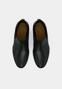 Botines de cuero negro con acabado liso, paneles laterales elásticos y suelas texturizadas. Presentan un diseño de punta redondeada con lengüetas para facilitar el calzado.