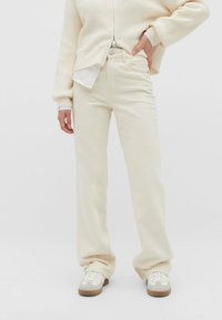 Jean droit de couleur crème en denim, présentant une fermeture à bouton, un design à cinq poches et une finition texturée subtile.