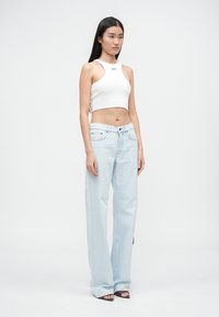 Top corto blanco con el texto "OFF", combinado con unos jeans ligeros de corte suelto en azul claro. Los jeans tienen bolsillos frontales y un cierre con cremallera.