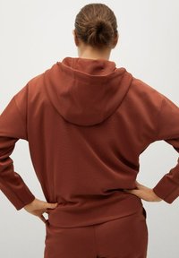 Brązowa bluza z kapturem wykonana z teksturowanej tkaniny, o luźnym kroju i bocznych kieszeniach. Zaprojektowana z klasycznym długim rękawem i ściągaczami przy mankietach.