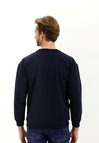 Sudadera azul marino de manga larga con puños acanalados, que presenta un cuello redondo clásico y un corte holgado. La vista trasera muestra un diseño sencillo.