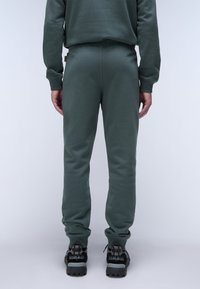 Grüne Sweatpants aus weichem Material, mit einer figurbetonten Passform und gerippten Bündchen, kombiniert mit schwarzen robusten Sneakers.