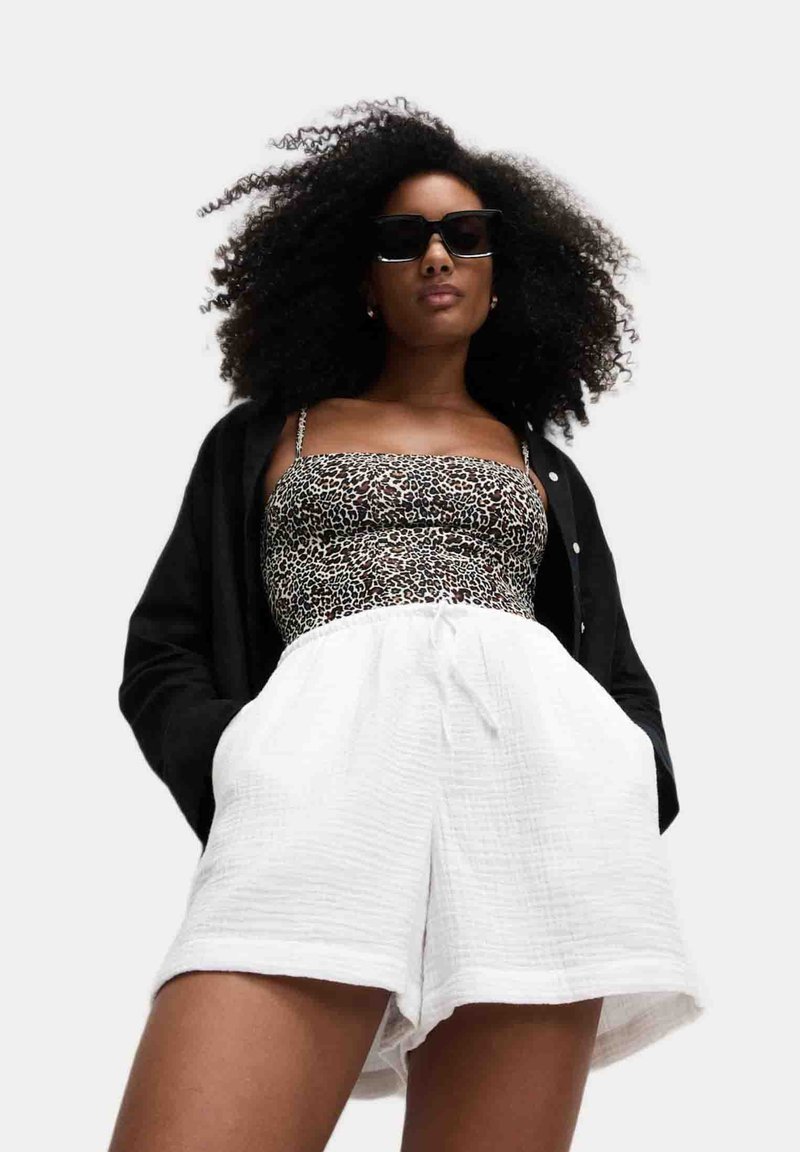 Veste noire à boutons, top à imprimé léopard et short blanc texturé avec poches. La tenue présente une coupe décontractée et des bretelles réglables.