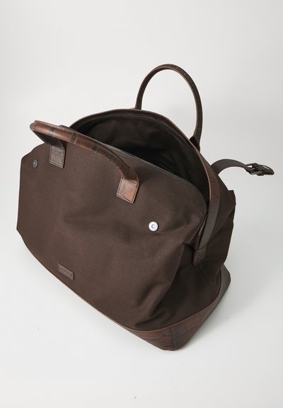 Brown canvas bag with dark leather accents, featuring rounded handles, a zipper closure, and a spacious interior.
