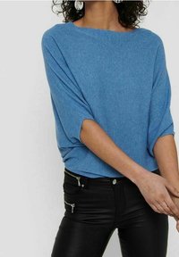 Pull bleu clair côtelé avec col large et manches courtes, associé à un pantalon noir ajusté avec des accents zippés.