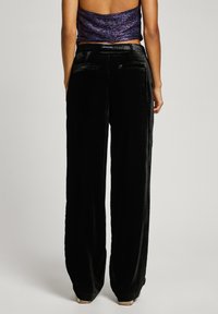 Svarta sammetsbyxor med vida ben och en slät yta, med två bakfickor och en subtil lyster, stylade med en figursydd lila crop top.