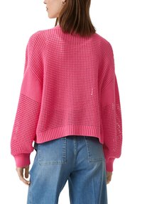 Różowy sweter dzianinowy o luźnym kroju, z teksturowanym wzorem i prążkowanymi mankietami. Połączony z niebieskimi jeansami o wysokim stanem.