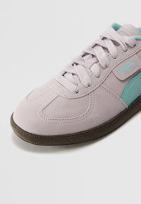 Light purple suede sneaker with turquoise accents, flat lace design, rubber sole, and stitched detailing along the sides.