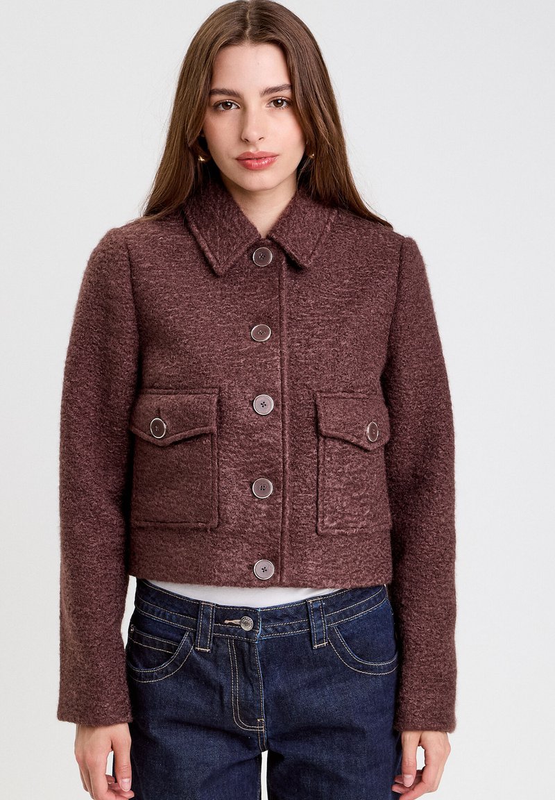 Braune kurze Jacke aus strukturiertem Stoff, mit einem Kragen, Knopfverschluss und zwei aufgesetzten Taschen vorne.