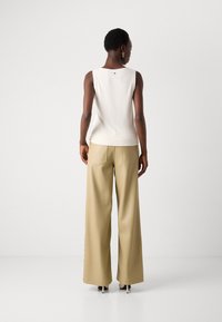 Top sans manches beige clair avec un ourlet côtelé, associé à un pantalon large marron clair. L'ensemble présente des détails de couture subtils et a un style minimaliste.