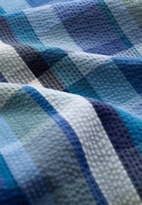 Textured fabric featuring a checkered pattern in various shades of blue, light blue, and white, displaying a rippled surface and soft texture.