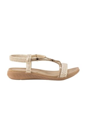 Sandalia plana beige con correa elástica en el tobillo, tira frontal trenzada y suela marrón texturizada diseñada para uso casual.