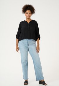 Blusa negra de corte holgado con escote en V y tres botones, combinada con vaqueros de talle alto en azul claro y sandalias negras de tacón cuadrado.