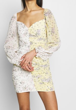 Robe mini florale avec un décolleté en cœur, présentant un côté texturé blanc et un motif floral jaune, des manches bouffantes et des détails froncés.