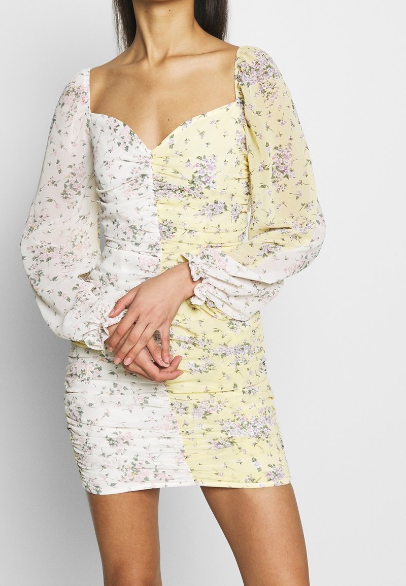 Vestido mini floral con escote corazón, que presenta un lado texturizado blanco y un patrón floral amarillo, mangas abullonadas y detalles fruncidos.