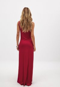 Robe maxi longue, sans manches, en rouge, fabriquée en tissu lisse, présentant une silhouette ajustée qui descend jusqu'au sol, avec des accents minimaux.