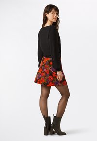 Sort tekstureret sweater og en flerfarvet blomster A-line nederdel. Outfittet er parret med sorte ankelstøvler og gennemsigtige sorte strømpebukser.