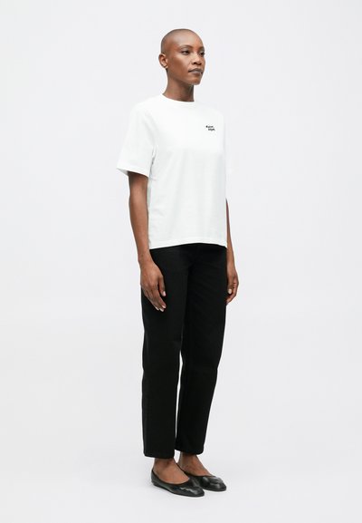 Tricou alb din bumbac cu mâneci scurte, având un mic logo negru. Asortat cu pantaloni negri drepti și balerini negri.