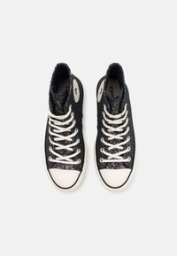 Höga sneakers med ett övre i svart och metallisk glittrande tyg, vita snören och gummihätta. Har cirkulära logopatchar på sidorna.