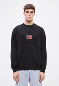 Μαύρο φούτερ με στρογγυλή λαιμόκοψη και ριμπ μανσέτες, με ορθογώνιο λογότυπο σε κόκκινο και μαύρο στο στήθος.