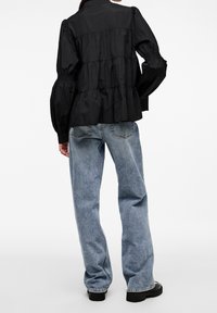 Blusa nera a balze con maniche puff strutturate, abbinata a jeans azzurri chiari a taglio morbido con una texture sfumata e cuciture visibili.