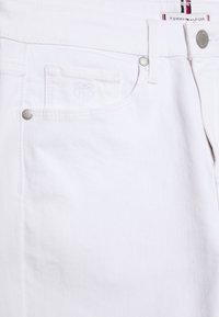 Pantalones vaqueros de mezclilla blanca que presentan un pequeño bolsillo para monedas, un sutil estampado del logo, herrajes metálicos y costuras en contraste a lo largo de las costuras.