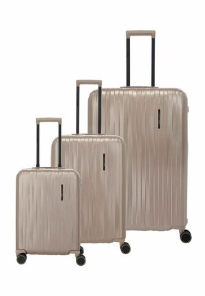 Tre valigie rigide beige di piccole, medie e grandi dimensioni con manici telescopici estesi e quattro ruote nere ciascuna.