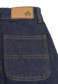 Denim jeans back pocket in dark blue with yellow stitching; features a brown leather label with the initials "B R" and crossed utensils design.