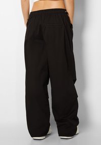 Baggy svarta byxor med elastisk midja, sidofickor och en mjuk tygkvalitet; har en enkel, funktionell design.